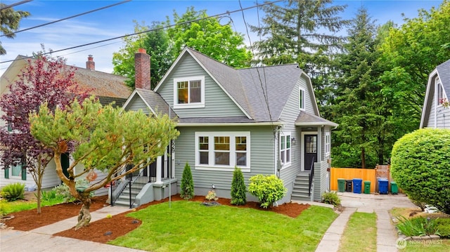 bungalow-style house with roof with shingles, a front yard, and a chimney