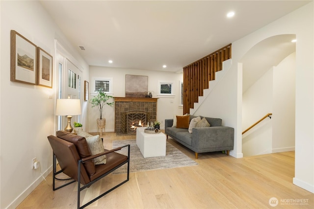 living room featuring wood finished floors, a lit fireplace, recessed lighting, baseboards, and stairs
