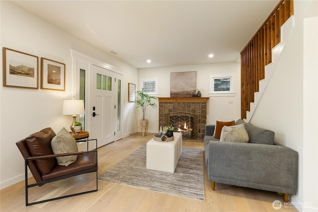 living room featuring stairs, wood finished floors, a warm lit fireplace, recessed lighting, and baseboards