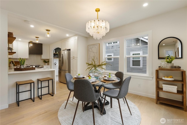 dining space featuring light wood-type flooring, arched walkways, a chandelier, recessed lighting, and baseboards