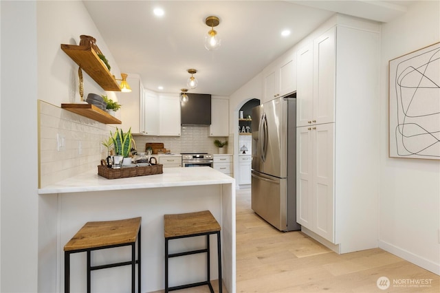 kitchen with appliances with stainless steel finishes, open shelves, white cabinets, a peninsula, and light wood finished floors