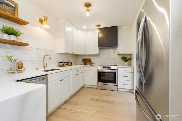 kitchen featuring appliances with stainless steel finishes, a sink, wall chimney exhaust hood, open shelves, and light wood-style flooring