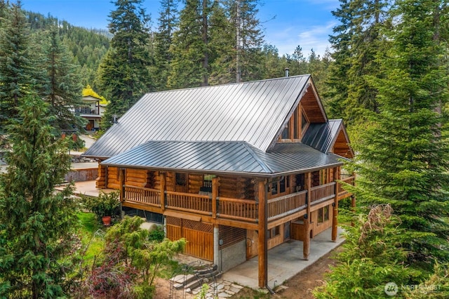 back of house with log exterior, a patio, a standing seam roof, and a wooded view
