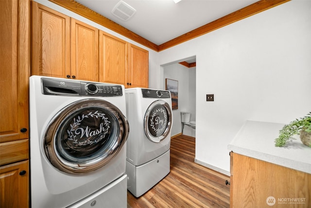 clothes washing area featuring separate washer and dryer, cabinet space, light wood-type flooring, crown molding, and baseboards