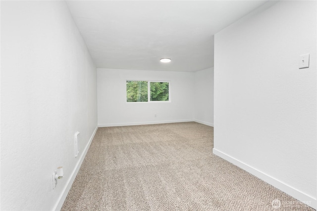 spare room featuring light colored carpet and baseboards