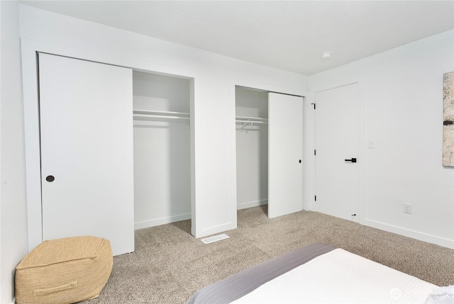 unfurnished bedroom with carpet floors, two closets, and baseboards