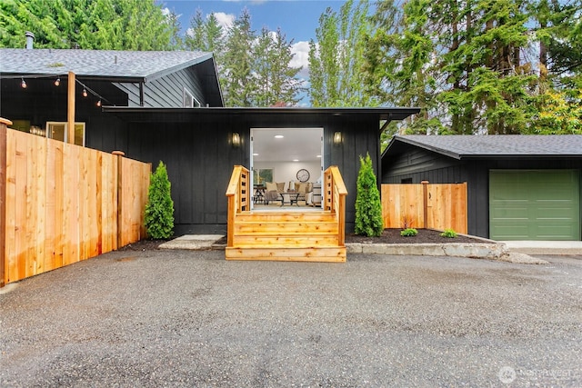 view of front of house featuring a shingled roof, fence, and a garage