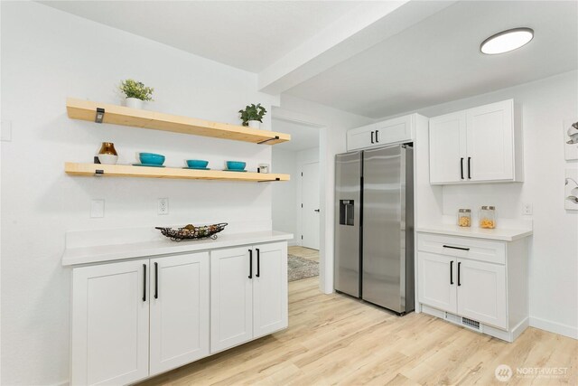 kitchen with stainless steel fridge with ice dispenser, light wood-style flooring, light countertops, and white cabinetry