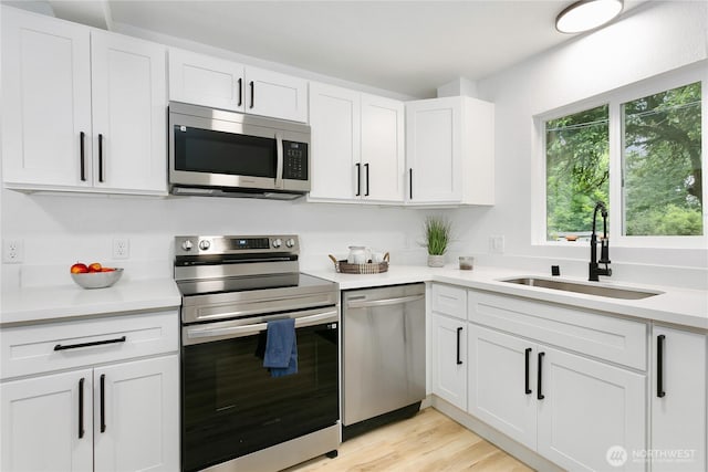 kitchen with appliances with stainless steel finishes, a sink, white cabinetry, light countertops, and light wood-style flooring