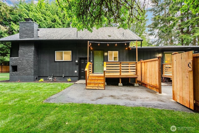 view of front of home featuring a chimney, roof with shingles, a front yard, and board and batten siding