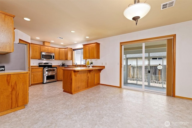 520 W Summer Breeze Ln, Sequim, WA 98382 - kitchen with appliances with stainless steel finishes, a peninsula, brown cabinetry, baseboards, and recessed lighting