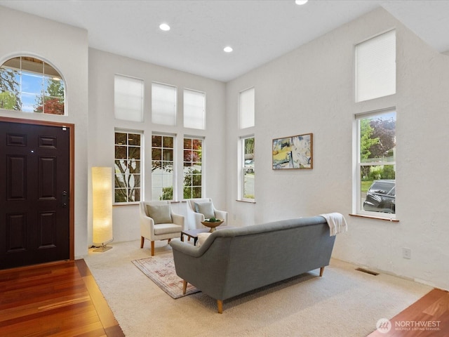 living area with healthy amount of natural light, recessed lighting, a high ceiling, and wood finished floors