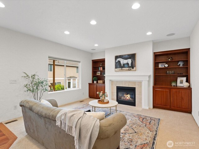 living area with a tiled fireplace, recessed lighting, carpet flooring, and built in shelves
