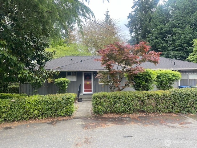 view of property hidden behind natural elements with roof with shingles