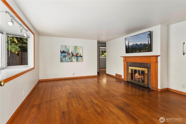 unfurnished living room with wood finished floors, a brick fireplace, and baseboards