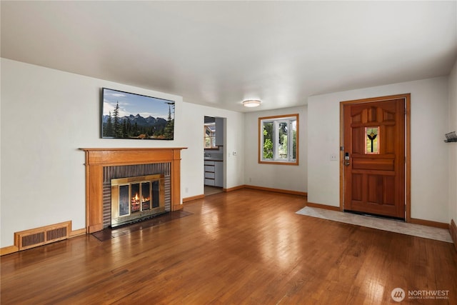 unfurnished living room with a brick fireplace, wood finished floors, and baseboards