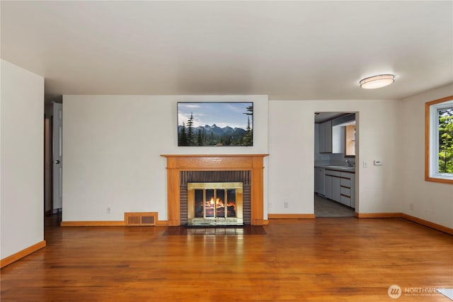unfurnished living room featuring a sink, wood finished floors, a fireplace, and baseboards