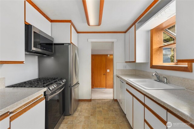 kitchen with appliances with stainless steel finishes, a sink, white cabinets, light countertops, and crown molding