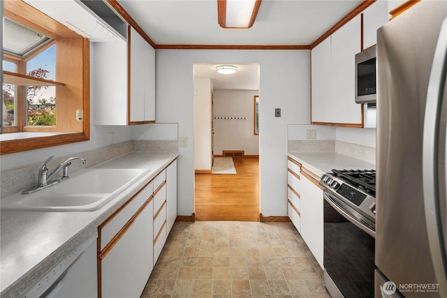 kitchen with stainless steel appliances, a sink, white cabinets, stone finish flooring, and light countertops
