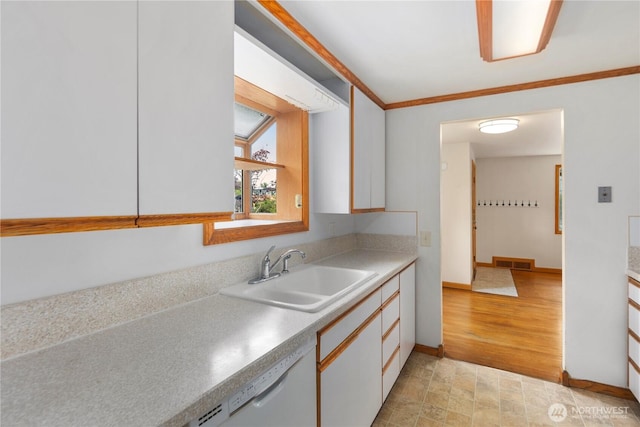 kitchen with a sink, dishwasher, white cabinets, light countertops, and baseboards