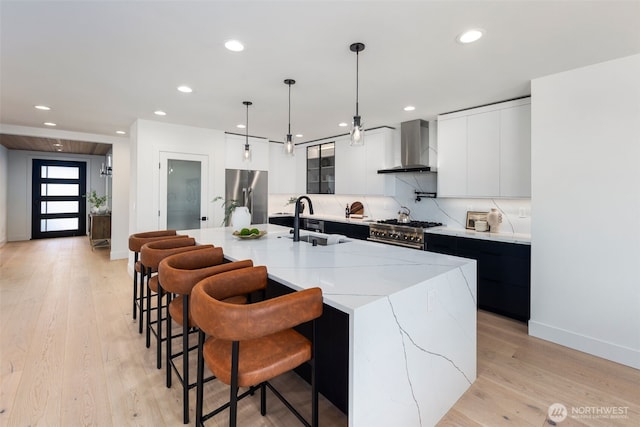 kitchen featuring wall chimney range hood, appliances with stainless steel finishes, a sink, modern cabinets, and recessed lighting