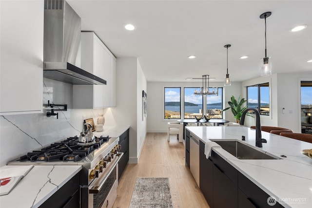 kitchen with wall chimney exhaust hood, stainless steel range, dark cabinets, a sink, and light stone countertops