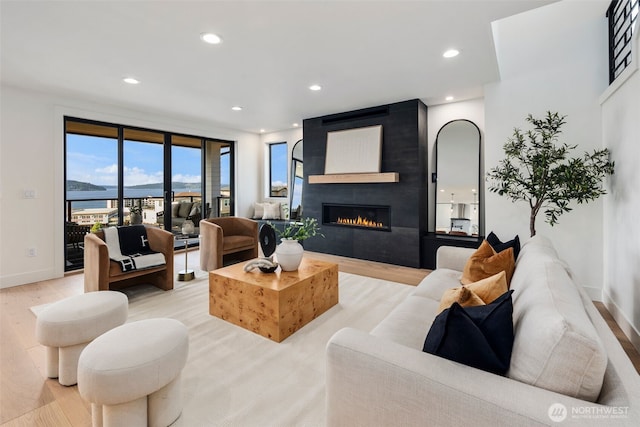 living room featuring light wood-style floors, a large fireplace, recessed lighting, baseboards, and a water view