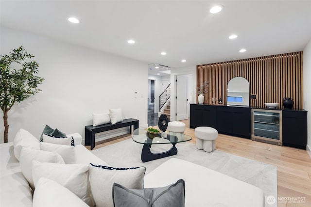 living room with beverage cooler, stairway, light wood finished floors, recessed lighting, and bar