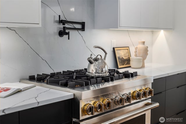 kitchen view of modern cabinets, high end stove, light stone counters, and pot filler