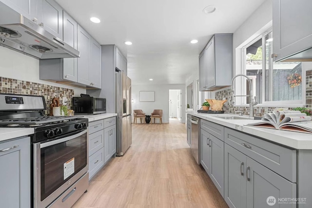 kitchen featuring appliances with stainless steel finishes, gray cabinets, under cabinet range hood, a sink, and light countertops