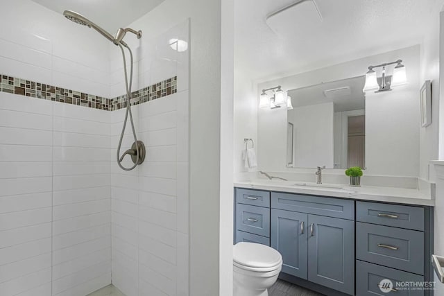 bathroom featuring toilet, tiled shower, and vanity