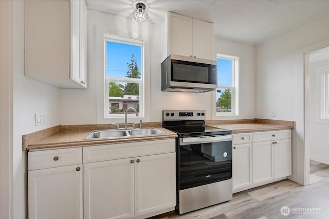 kitchen with stainless steel appliances, a sink, white cabinetry, light wood-type flooring, and light countertops