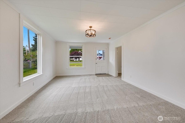 spare room featuring a chandelier, light colored carpet, baseboards, and crown molding