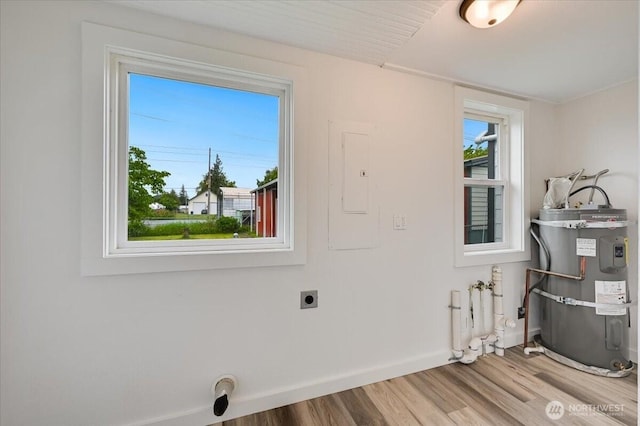 clothes washing area with hookup for an electric dryer, strapped water heater, wood finished floors, and baseboards