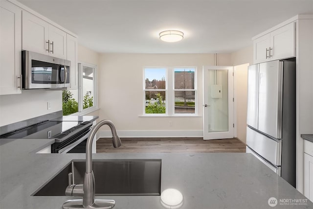 816 N 43rd St, Seattle, WA 98103 - kitchen featuring appliances with stainless steel finishes, white cabinets, wood finished floors, a sink, and light stone counters