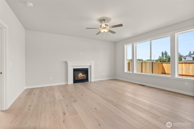 2880 75th Ave SW Lot 62, Tumwater, WA 98512 - unfurnished living room featuring light wood-style floors, a ceiling fan, a glass covered fireplace, and plenty of natural light