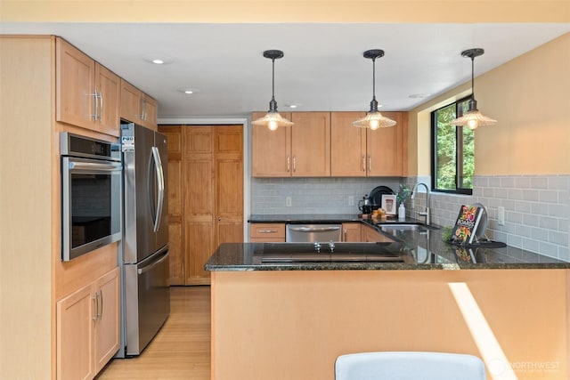 kitchen featuring a sink, appliances with stainless steel finishes, a peninsula, light wood-style floors, and decorative backsplash