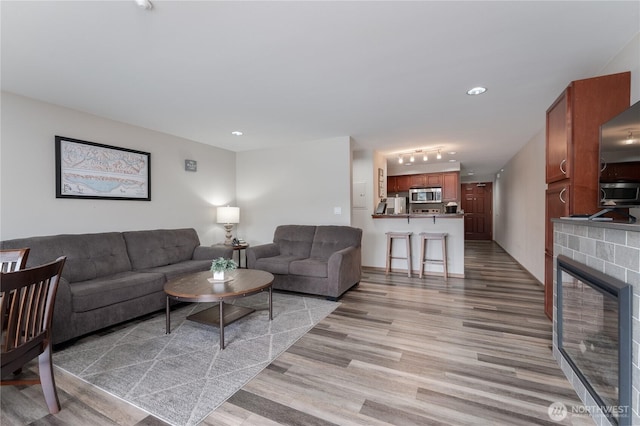 living area with light wood-style floors, a glass covered fireplace, and recessed lighting