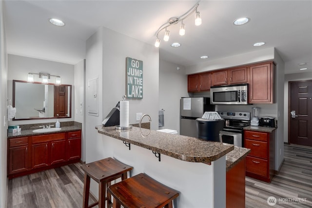 kitchen featuring appliances with stainless steel finishes, a sink, light wood-style flooring, a kitchen bar, and a peninsula