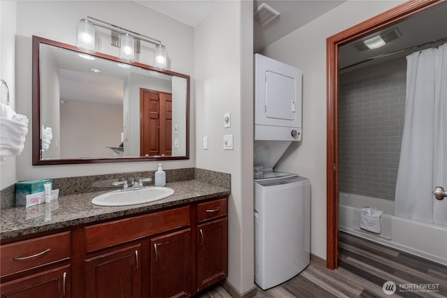 full bathroom featuring stacked washer / dryer, wood finished floors, vanity, and shower / bath combo with shower curtain