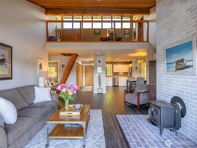 living area featuring a wood stove, a high ceiling, dark wood-style flooring, and stairway