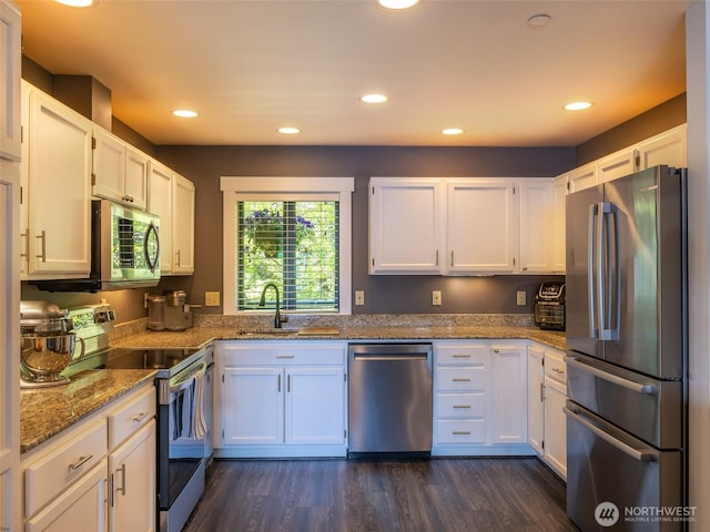 kitchen with stainless steel appliances, a sink, white cabinets, stone countertops, and dark wood finished floors