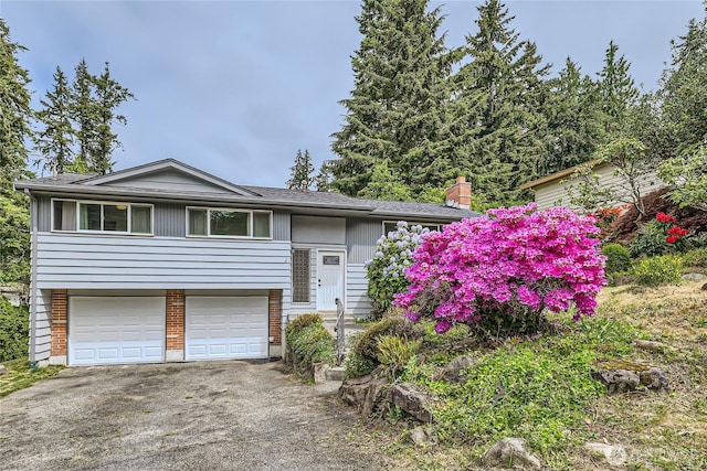 raised ranch with asphalt driveway, an attached garage, and a chimney