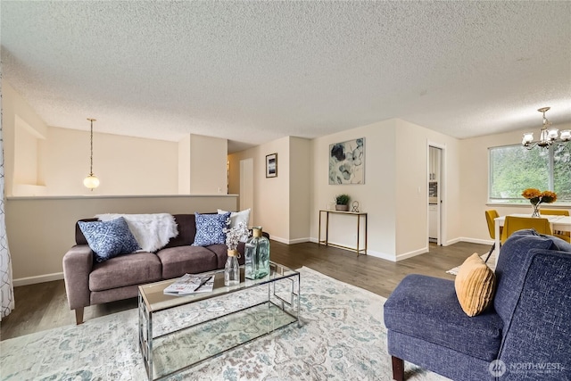 living area featuring a chandelier, dark wood-style flooring, a textured ceiling, and baseboards