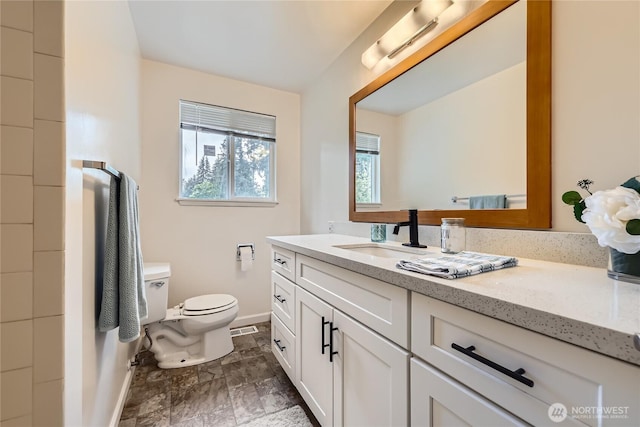 bathroom with baseboards, toilet, vanity, and stone finish floors