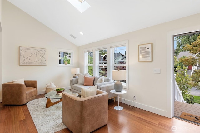 living area featuring baseboards, plenty of natural light, light wood finished floors, vaulted ceiling, and a skylight