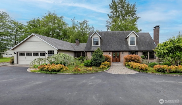 cape cod home with a chimney, driveway, brick siding, and french doors