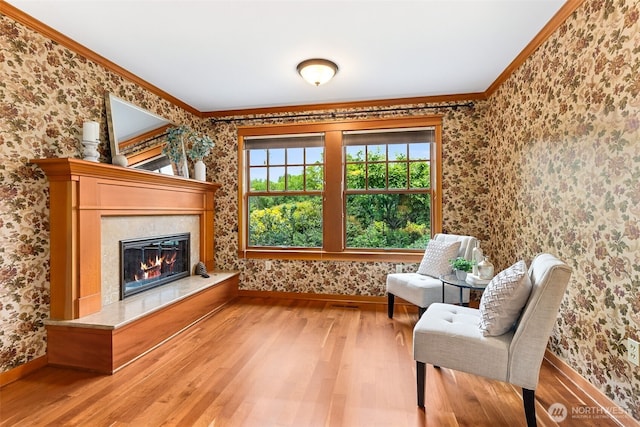 sitting room with wallpapered walls, baseboards, wood finished floors, ornamental molding, and a fireplace