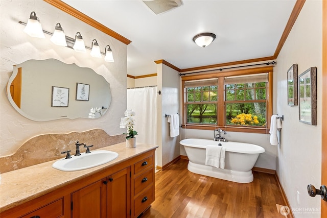 full bathroom featuring wood finished floors, vanity, baseboards, crown molding, and a freestanding tub