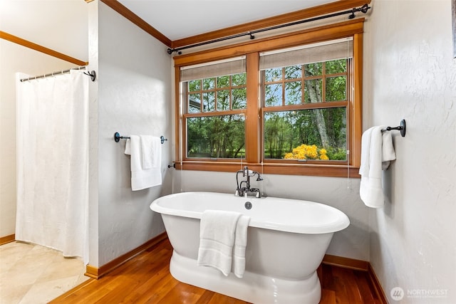 bathroom with baseboards, wood finished floors, a soaking tub, a shower with curtain, and crown molding